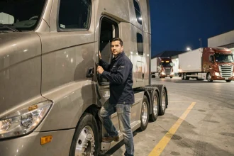 Chauffeur poids lourd de nuit montant dans la cabine de son camion dans un dépôt logistique industriel